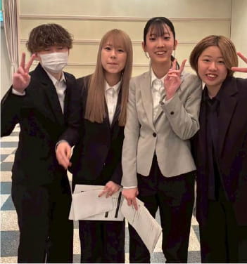 スーツ姿の4人が笑顔でポーズを取る写真